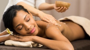 Spa therapist applying scrub salt on young woman back at salon spa