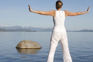 Attractive woman in white meditating by still water