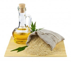 Macro view of sesame seeds in flax sack and glass bottle of sesame oil isolated on white background