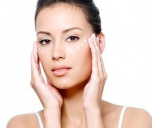 Close-up portrait of beautiful young woman's face with point of rejuvenating cream under the eyes - isolated