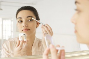 Young woman applying make-up in mirror, using brush, close-up